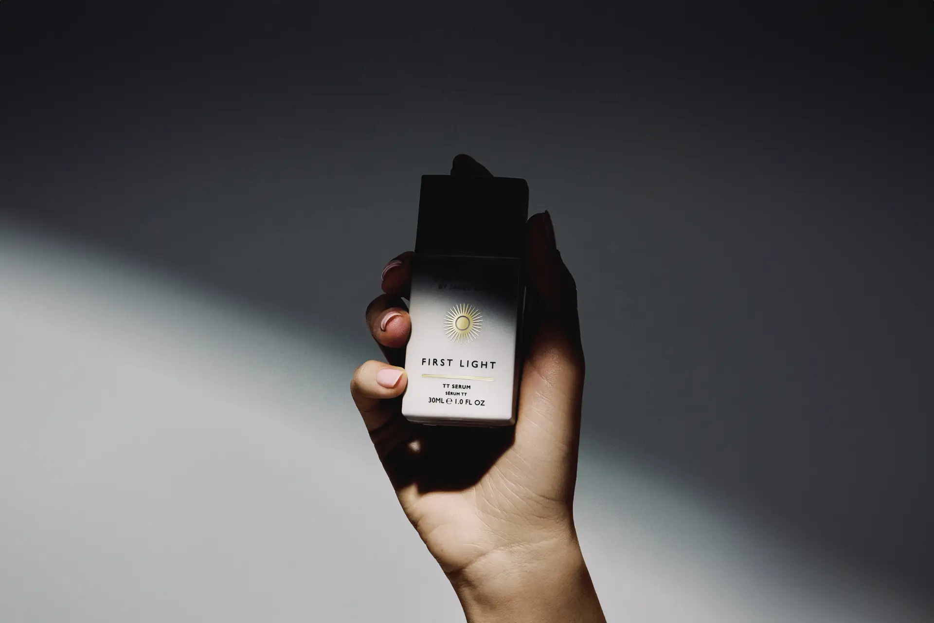 First Light serum bottle from Self Glow by James Read held in hand against dramatic light and shadow backdrop, art directed by Saltco